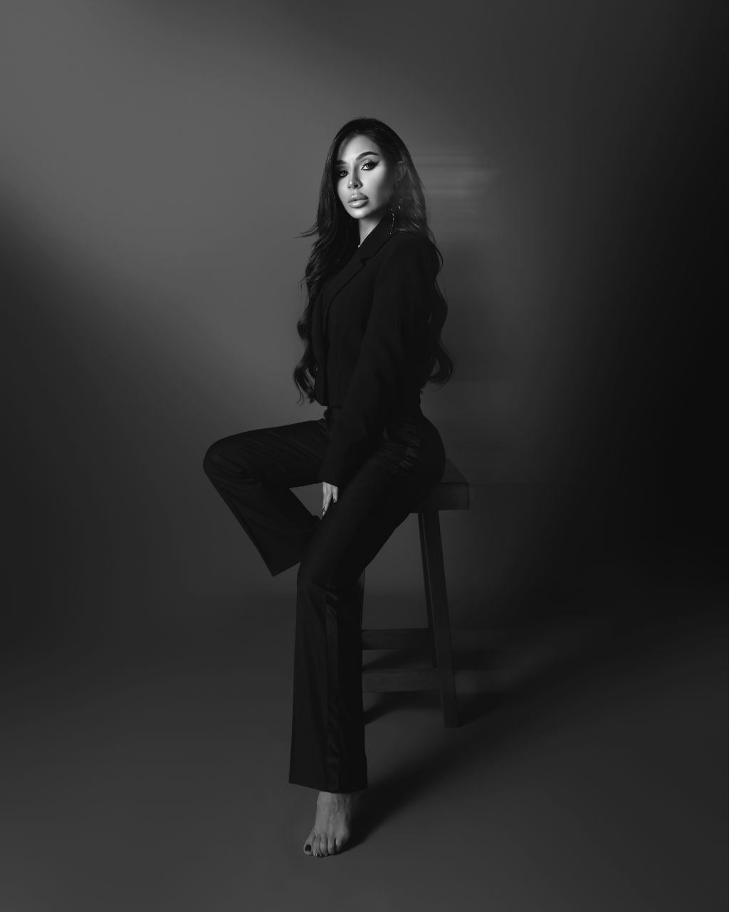 Black and white studio photograph of Zina Almokri seated on a stool