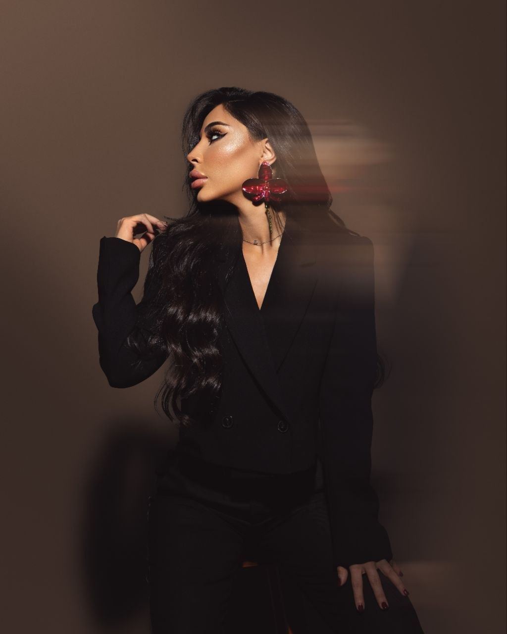 Studio portrait of Zina Almokri in a black blazer, turned in profile against a warm brown backdrop