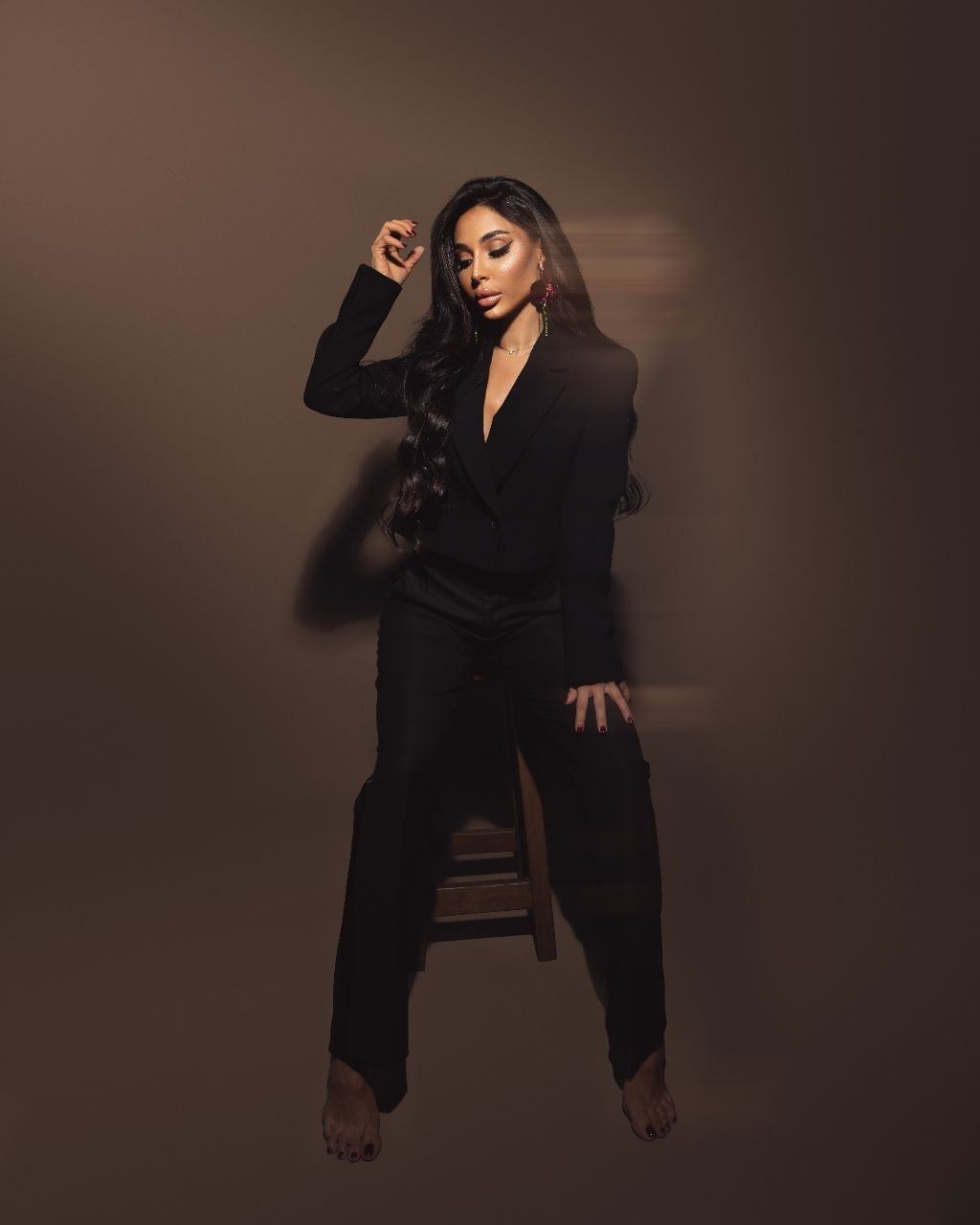 Studio photograph of Zina Almokri seated against a warm brown backdrop